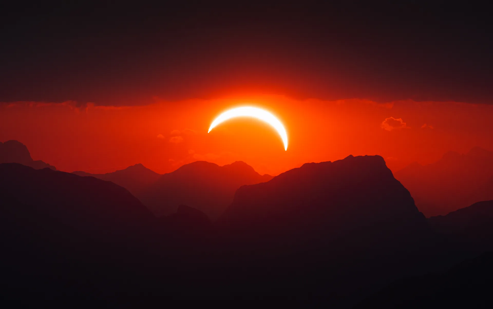 A crescent sun in partial eclipse above layered mountain silhouettes